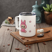 Pink Labubu monster with pink star pattern on a white mug on a table with coffee beans scattered
